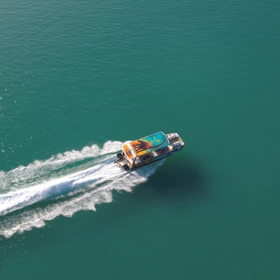 Aerial view of a speedboat creating a white wake on calm blue-green water.