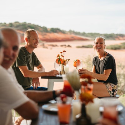 Group of people smiling and enjoying drinks outdoors with a desert landscape in the background.