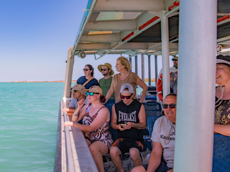 Group of people enjoying a scenic boat ride on a sunny day with blue water and sky.
