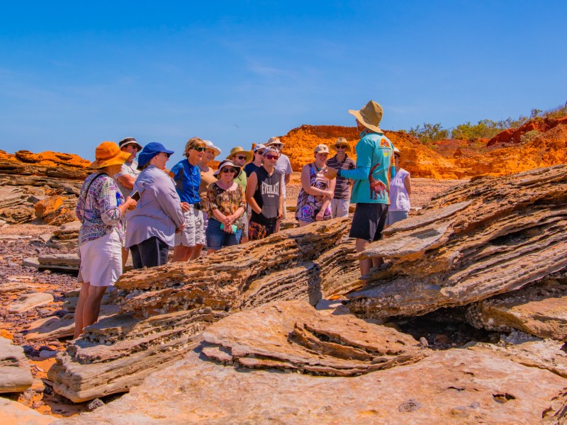 Tour guide speaking to a group of tourists on a rock formation under a clear blue sky.