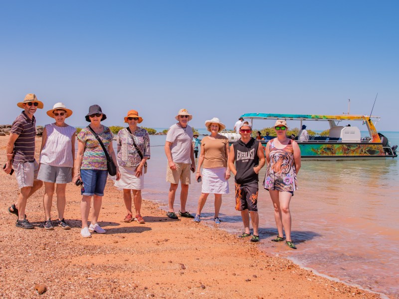 Group of people on a beach with a boat in the water.