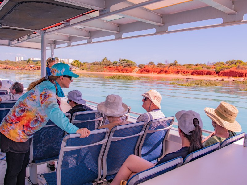 People on a boat tour wearing hats, with scenic red cliffs and water in the background.
