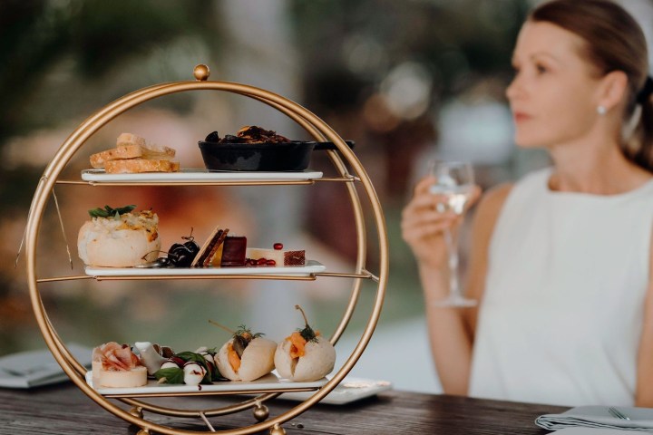 Woman at table with tiered platter of appetizers and a glass of wine.