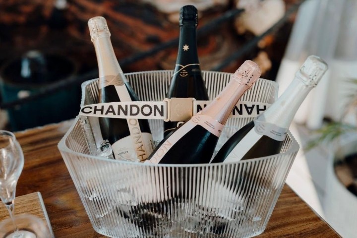 Five bottles of sparkling wine in an ice bucket on a wooden table.