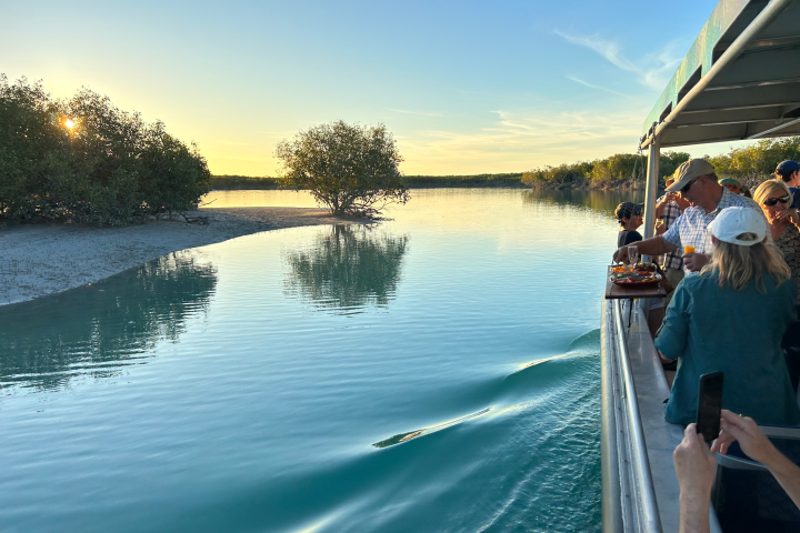 Tourists on a boat enjoying sunset near a tranquil river with trees.
