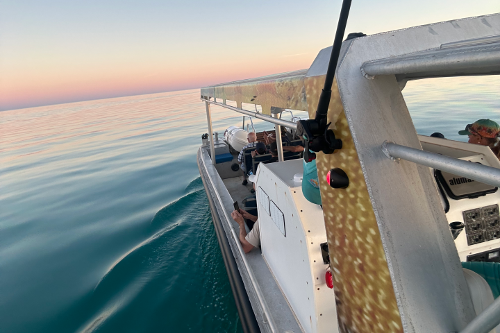 People on a boat enjoying calm waters during a pastel sunset.
