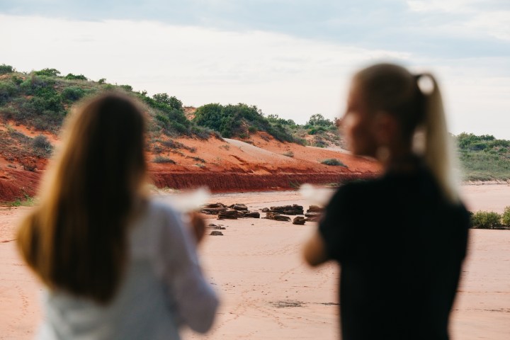 Two blurred people observing a red desert landscape with hills.