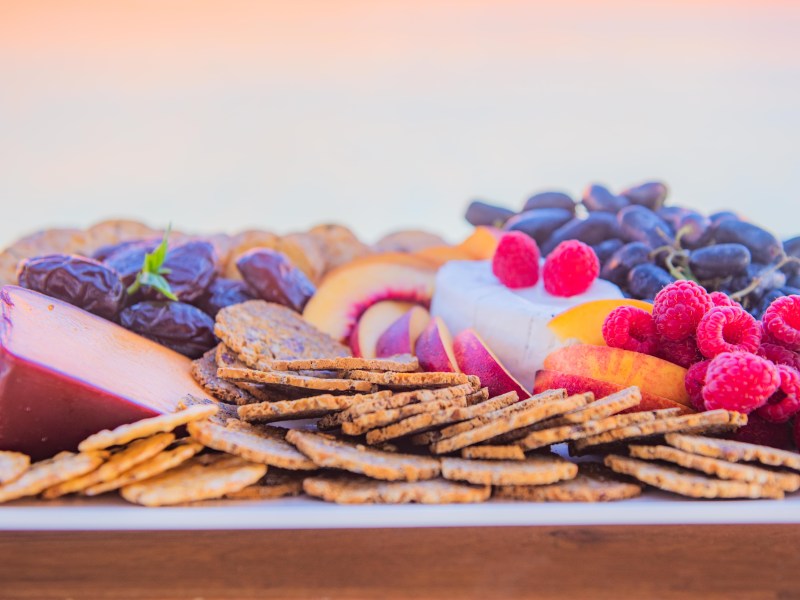 Assorted cheeses, crackers, grapes, raspberries, and peach slices on a platter.