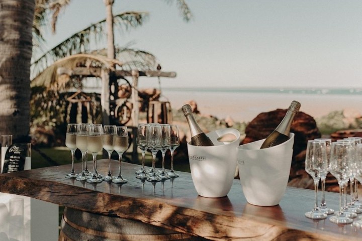 Outdoor bar setup with champagne bottles, glasses, palm trees, and ocean view.