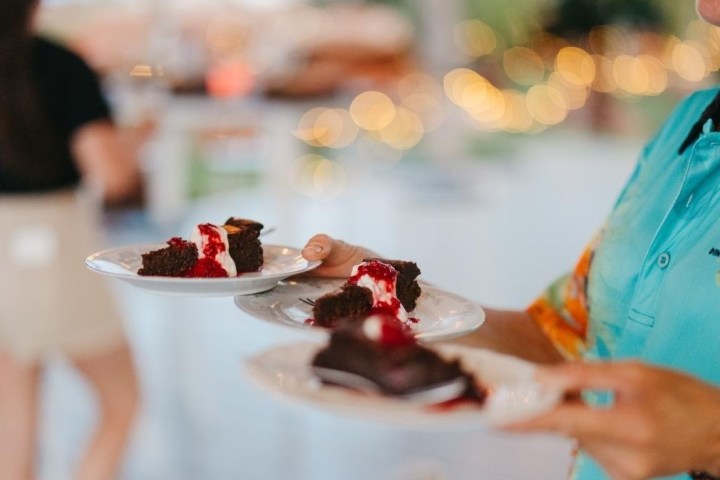 Person holding plates with chocolate cake slices and red sauce, wearing a blue uniform shirt.
