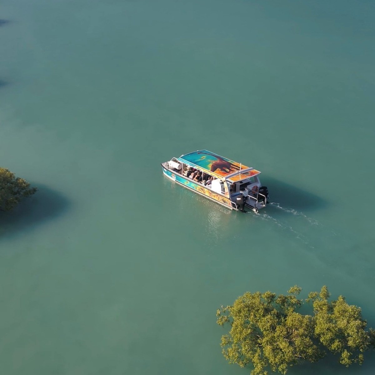 Aerial view of a boat navigating through a turquoise lake with small islands.