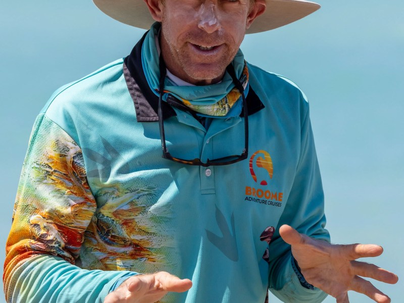 Person in wide-brimmed hat and colorful shirt gestures while standing outdoors.