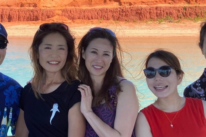 Five people smiling in front of red rock cliff and blue water.