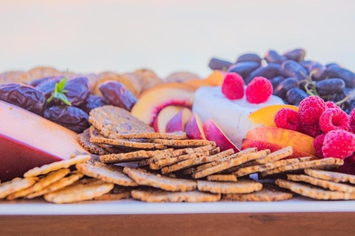 Cheese platter with assorted crackers, fruits, and berries on a white plate.