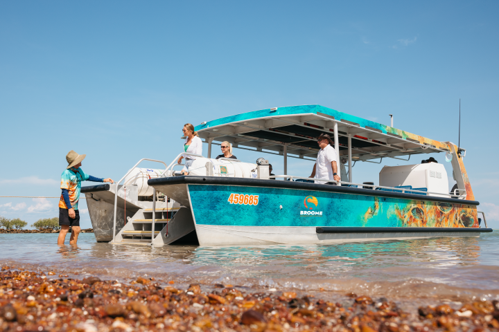 Tourists on a colorful boat at a beach, with one person on the shore.
