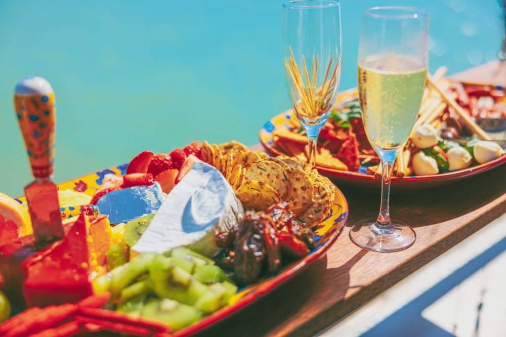 Colorful fruit and cheese platter with champagne glasses by the water.