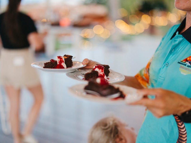 Person serving chocolate cake slices with sauce on plates.