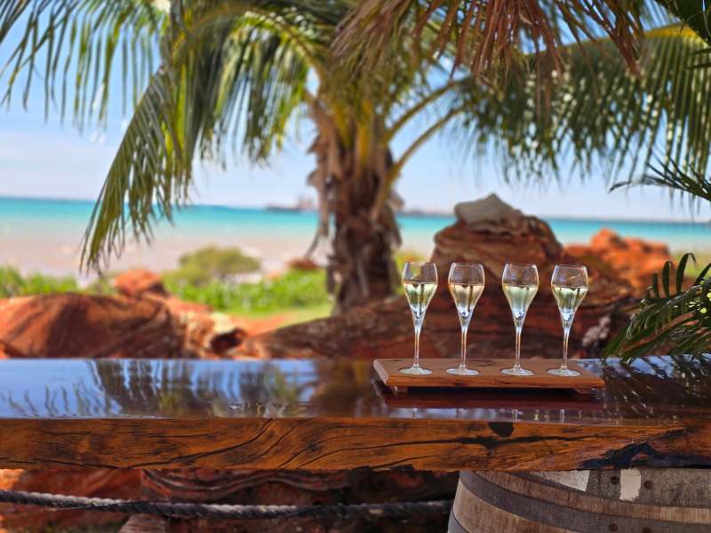 Four glasses on wooden table by tropical beach with palm trees.